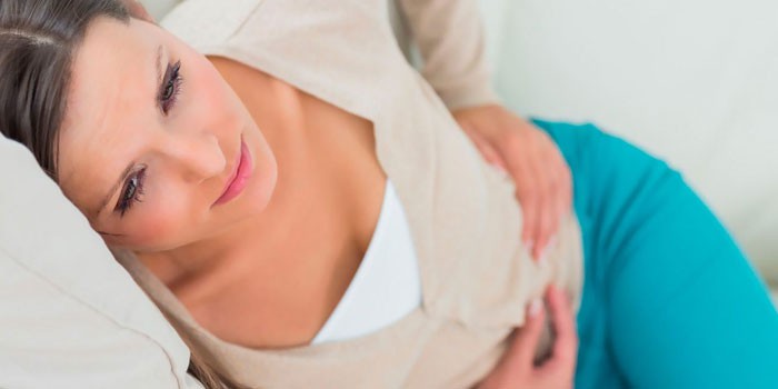 Девушка лежит на диване и держится руками за живот